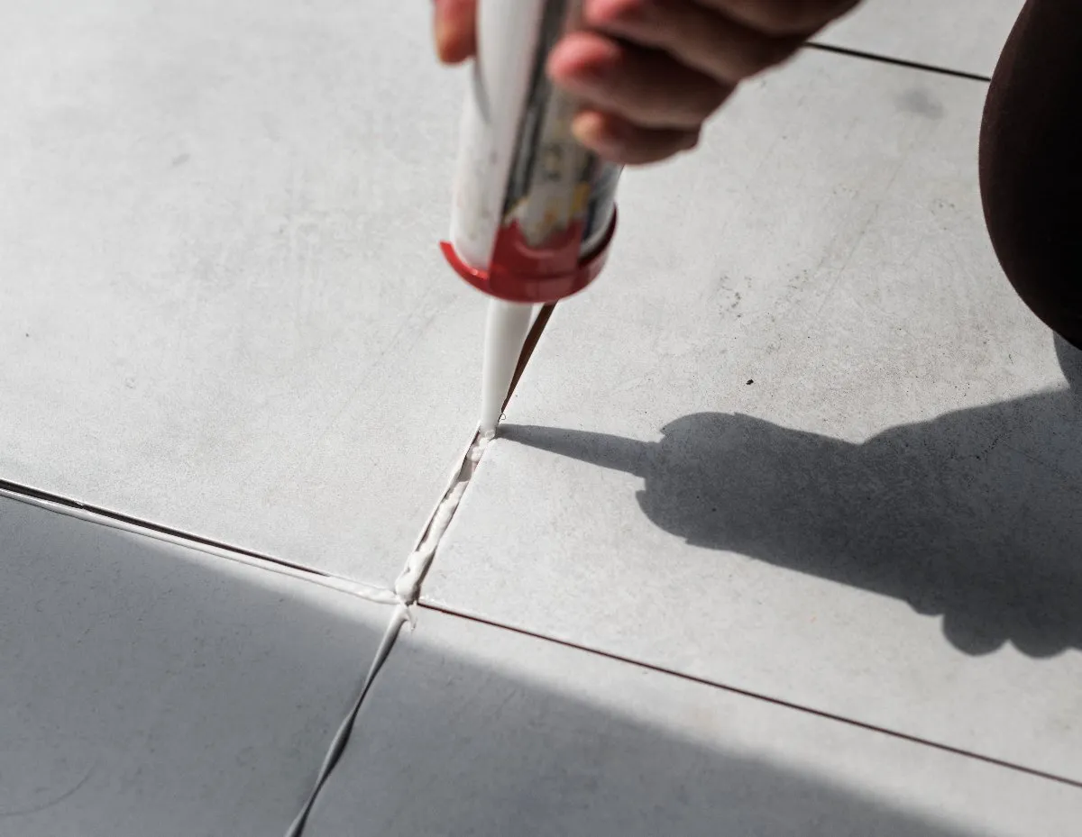 A person carefully uses a glue gun to fix a broken tile, demonstrating focus and craftsmanship in their repair work.